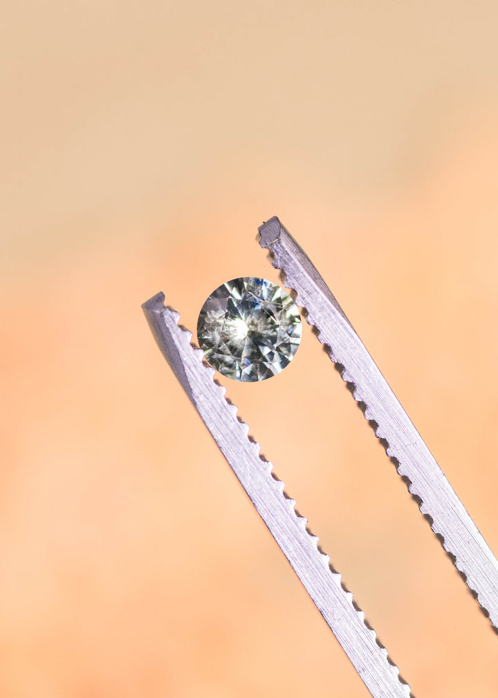 Loose teal and green Montana sapphire pair held in tweezers, highlighting the round brilliant cut and lively natural color under soft light.