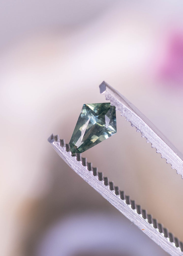 0.57ct teal blue green Montana sapphire kite step cut held in gem tweezers, rotating to display step facets, precision angles, and natural untreated brilliance