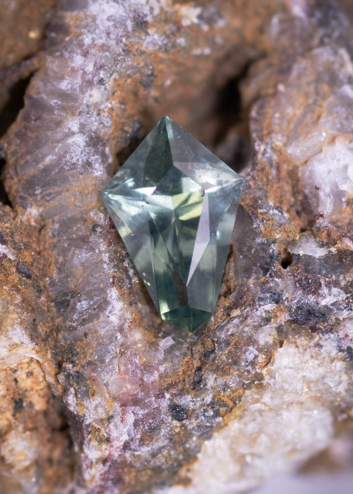 0.57 carat teal blue green Montana sapphire in kite step cut resting on natural quartz rock, showing sharp geometric facets and untreated clarity from El Dorado Bar Deposit