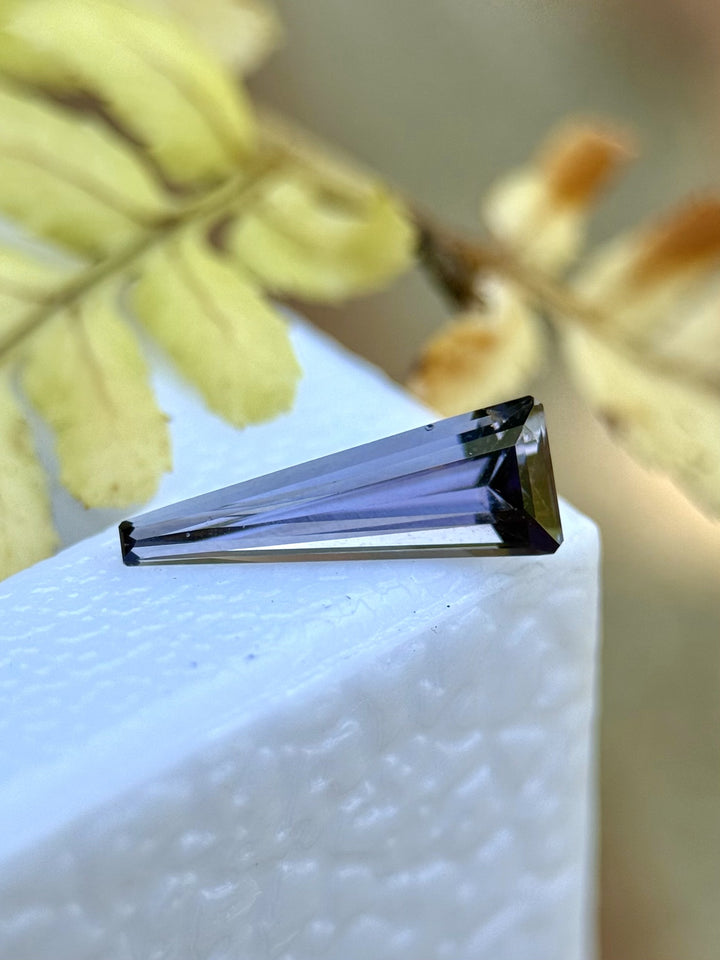 Side profile of a Tanzanite gemstone on a white display with earthy gray, peach, and lavender tones captured in its precision cut.