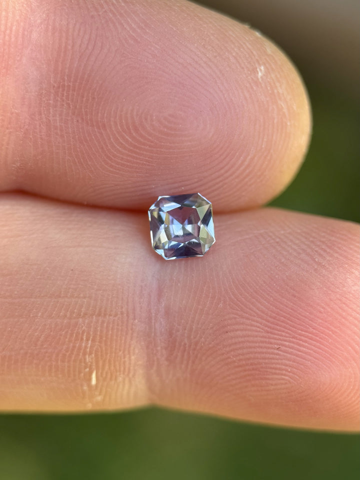 Natural 0.67ct color shift sapphire resting on fingertip, with visible lilac to blue color play – untreated Umba River gem