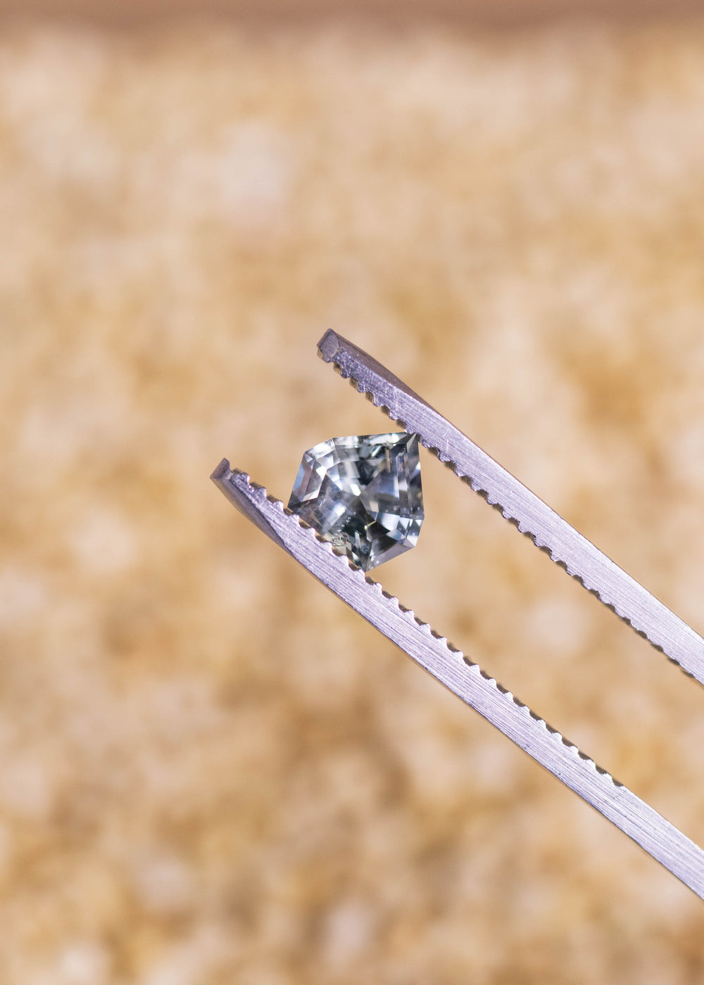 Loose green teal blue Montana sapphire held in tweezers, showing the geometric shield mix cut and clean faceting under natural light.