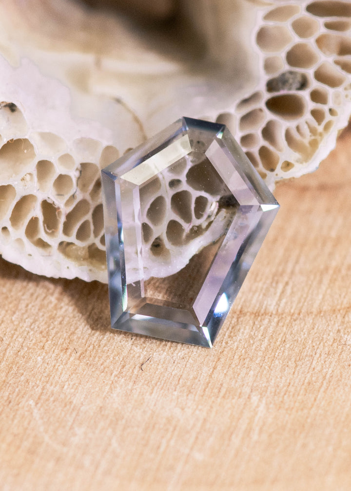 Loose green, blue and teal Montana sapphire shown face-up on a natural surface, displaying the geometric pentagon portrait cut and transparent step-like faceting.