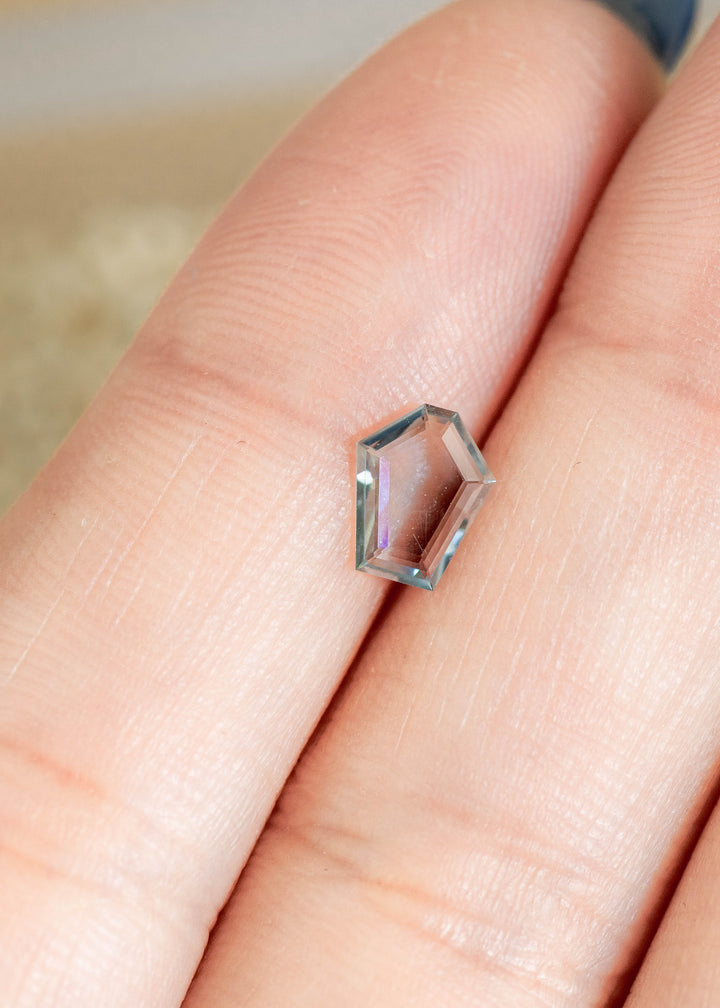 Loose green, blue and teal Montana sapphire resting on fingertips for scale, showing the flat portrait cut, crisp edges and natural unheated color.