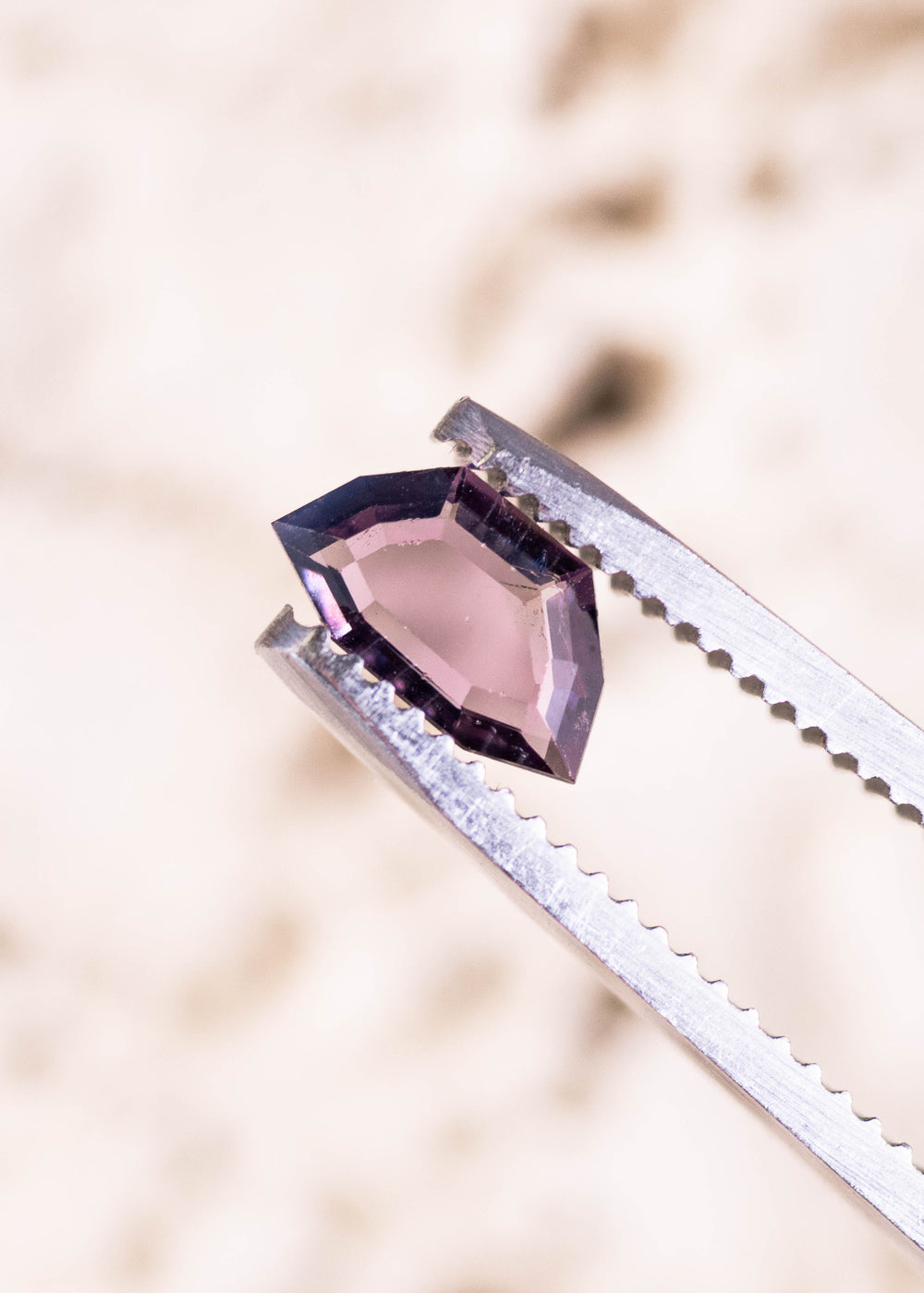 0.70ct purple pink Sri Lanka spinel held in tweezers, geometric step cut portrait displaying crisp step facets and elongated symmetrical shape