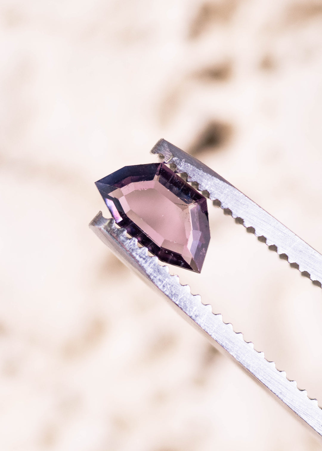 0.70ct purple pink Sri Lanka spinel held in tweezers, geometric step cut portrait displaying crisp step facets and elongated symmetrical shape