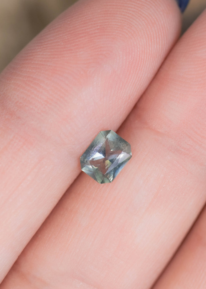 0.71 carat teal blue green sapphire displayed on finger for scale, unheated Montana gemstone with radiant mix cut and subtle color shift