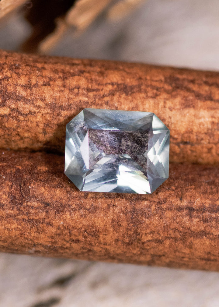 0.71 carat unheated Montana sapphire resting on natural wood, teal blue green radiant mix cut from El Dorado Bar Deposit with crisp geometric faceting