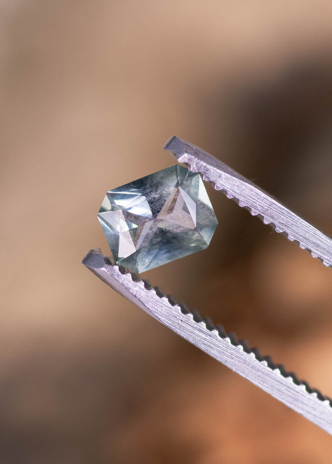 0.71ct teal blue green Montana sapphire held in tweezers, radiant mix cut gemstone showing natural brilliance and precise facet reflections from El Dorado Bar