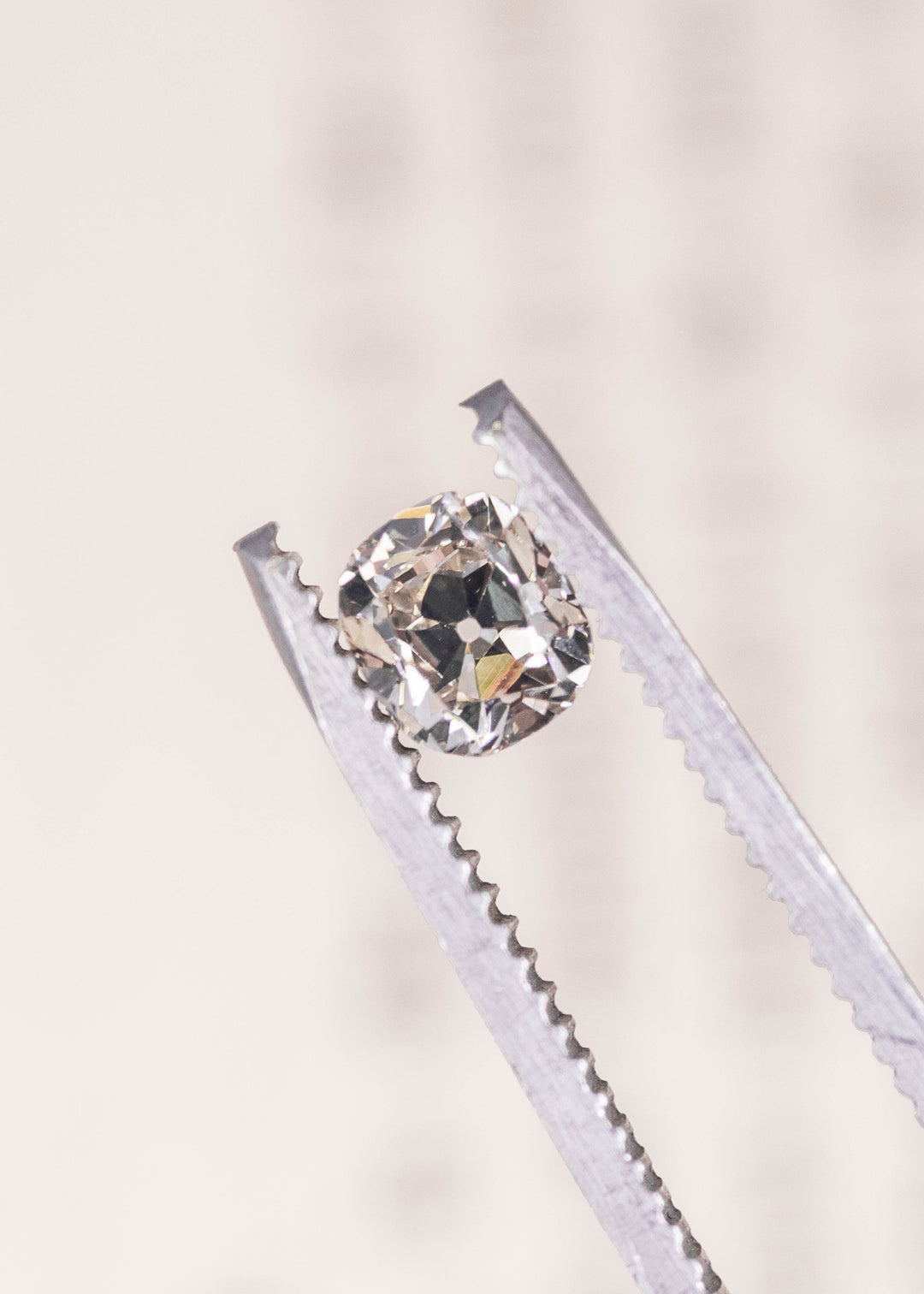 Loose 0.72 carat old mine cut cushion diamond held in tweezers showing antique faceting and soft champagne body color.