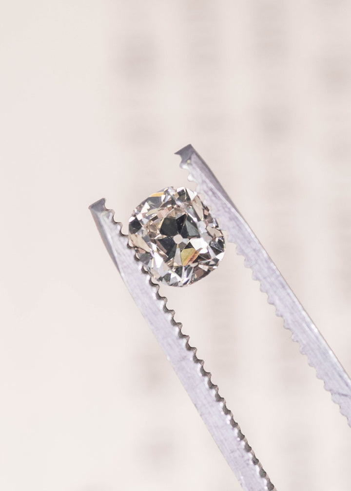 Loose 0.72 carat old mine cut cushion diamond held in tweezers showing antique faceting and soft champagne body color.