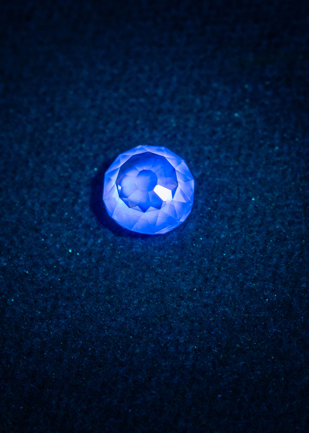 0.75 carat rosy champagne fancy light brown C4 diamond in Mughal cut glowing with very strong blue fluorescence under UV light, shown on a dark textured background to highlight the vivid fluorescent effect.