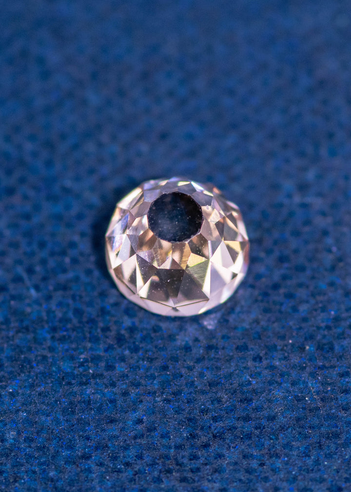 0.77 carat Fancy Light Brown C3–C4 Mughal cut diamond with VVS2 clarity and very strong blue fluorescence shown on a dark blue textured background, highlighting the concave faceting and round Mughal shape; natural diamond from South Africa, untreated.