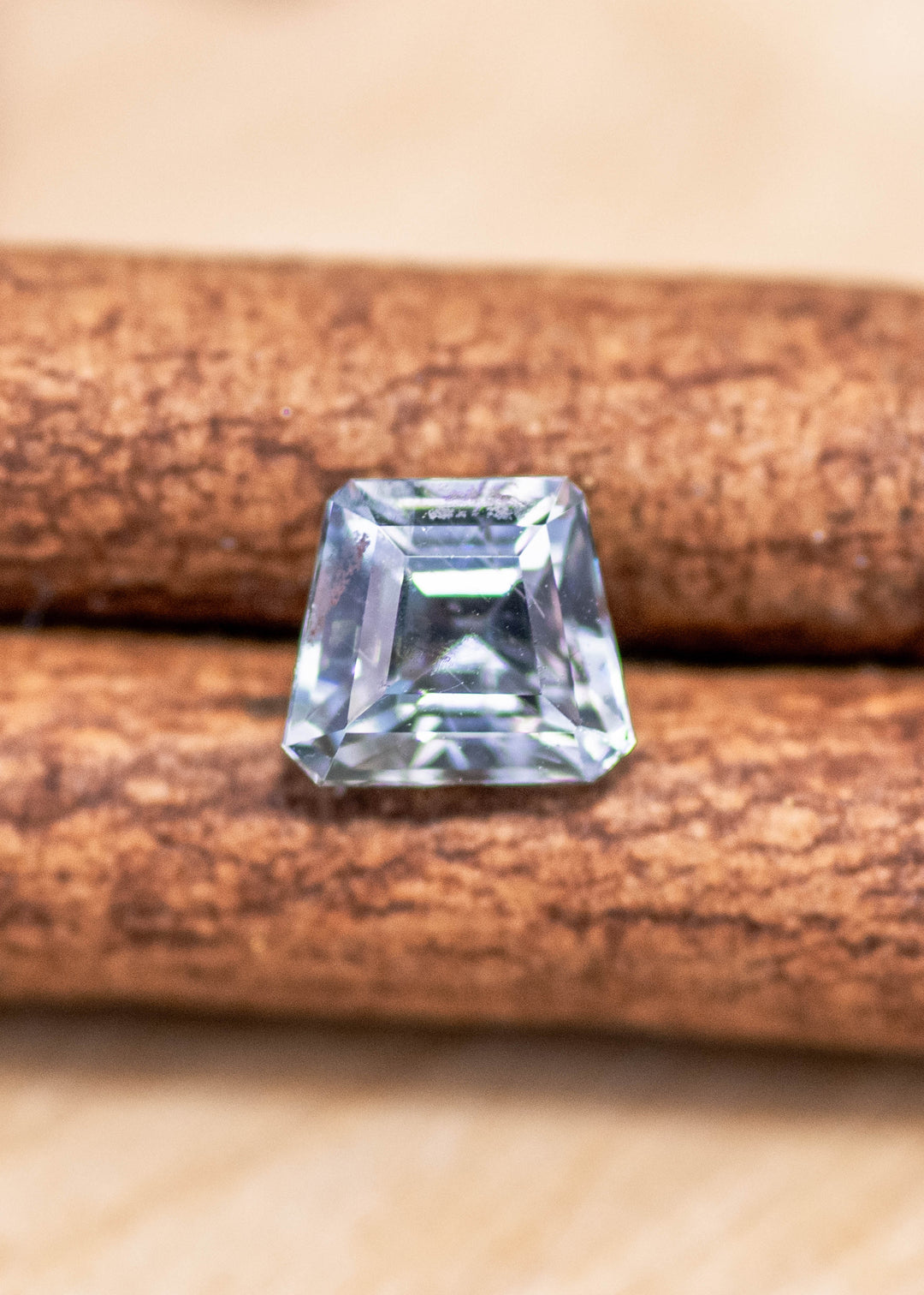 0.82ct seafoam Montana sapphire resting on a cinnamon stick, showing a pale mint-blue body color with sharp trapezoid outline and reflective step-cut facets.