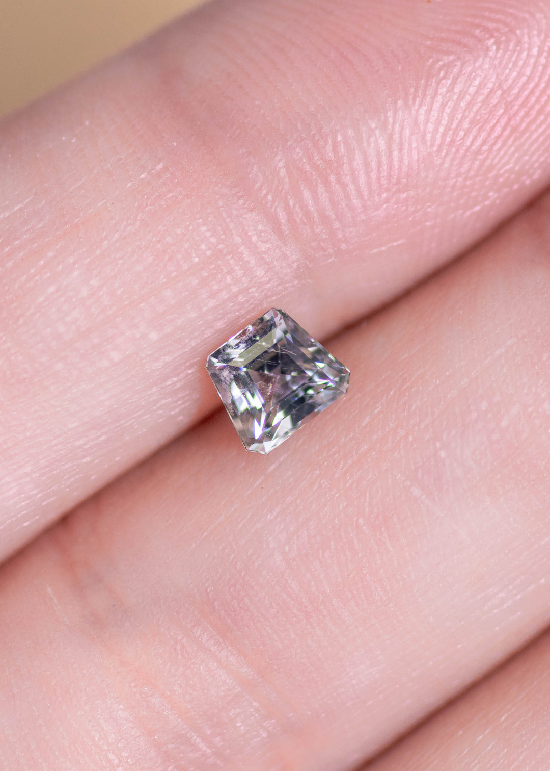 Small custom step cut seafoam sapphire displayed on fingertip, highlighting its delicate pastel green-blue color and crisp, angular silhouette.