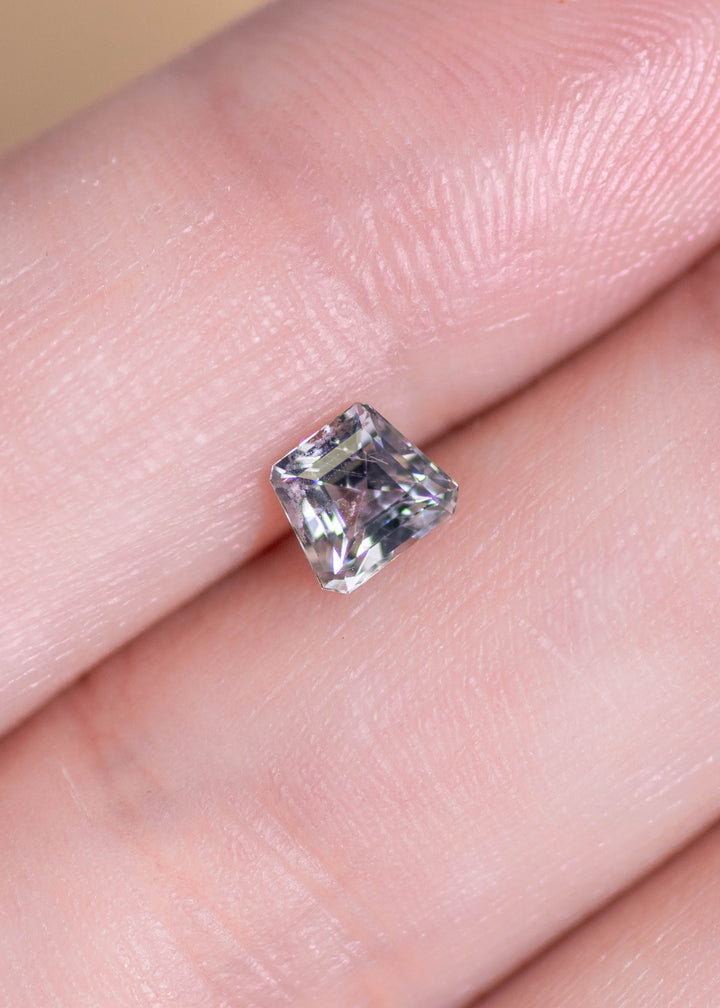 Small custom step cut seafoam sapphire displayed on fingertip, highlighting its delicate pastel green-blue color and crisp, angular silhouette.