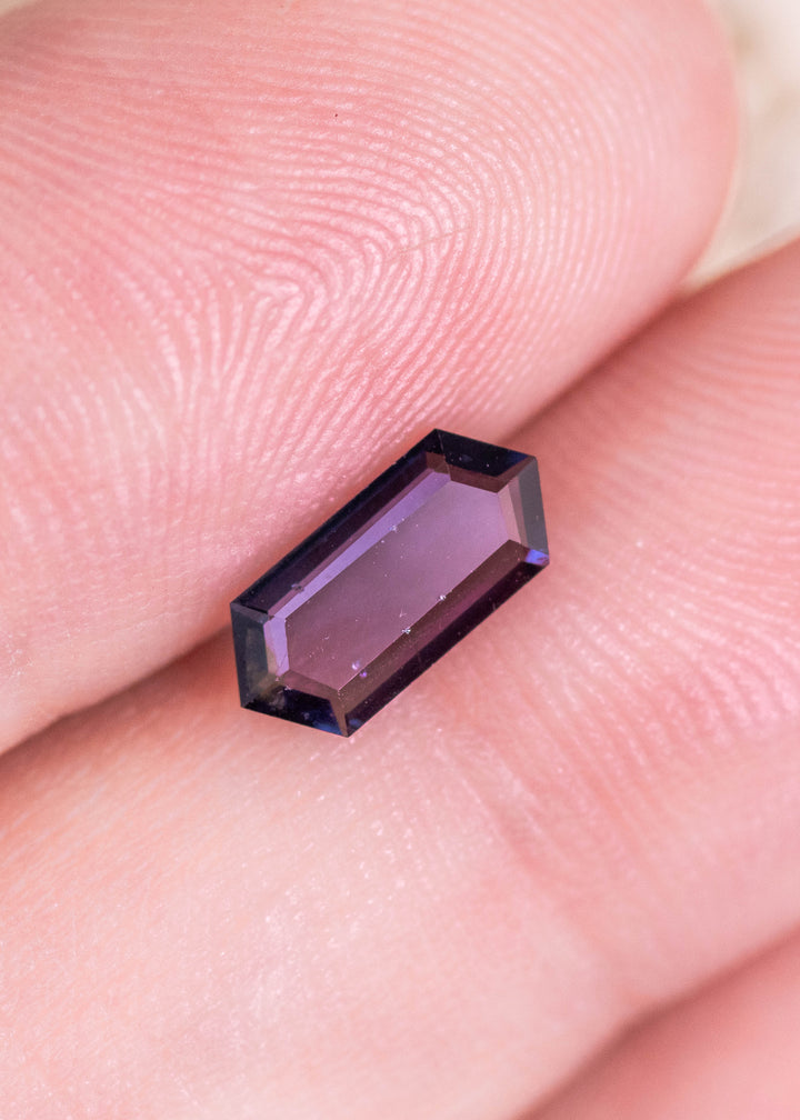 0.82 carat pink purple spinel displayed on finger for scale, unheated Sri Lanka gemstone with elongated hexagonal step cut portrait design