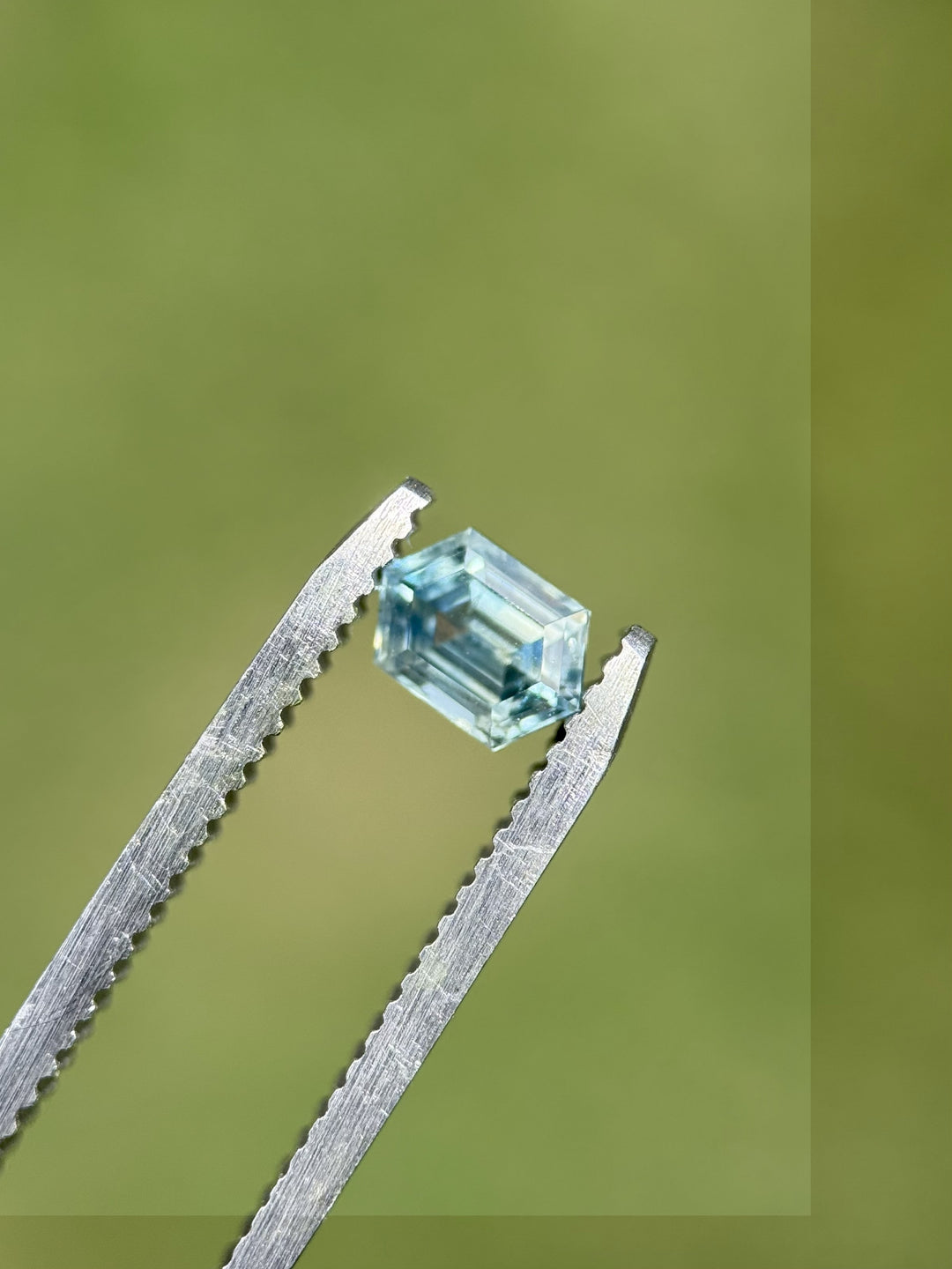 0.83ct Montana sapphire in hexagon step cut held in tweezers showing yellow, teal, and blue parti colors