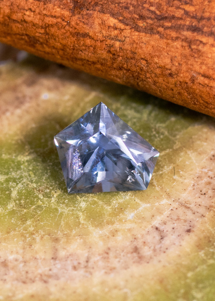 0.85 carat unheated Montana sapphire in a modified kite cut resting on natural stone surface, showing blue, green and violet color shift from El Dorado Bar Deposit.