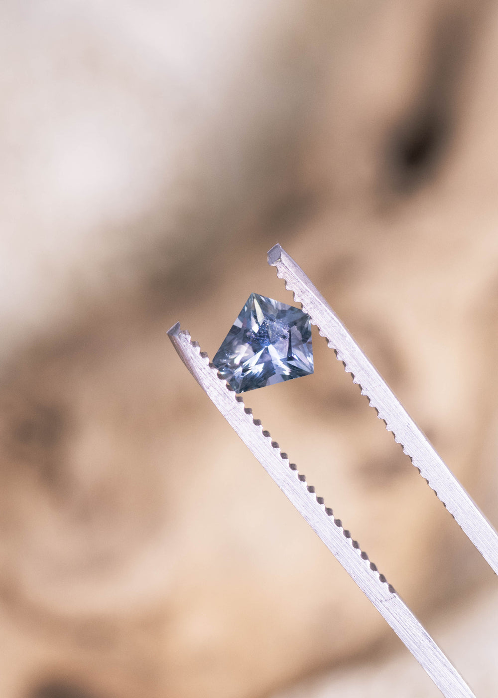 0.85ct blue green violet Montana sapphire held in jeweler’s tweezers, modified kite cut precision faceting reflecting light for custom jewelry design.