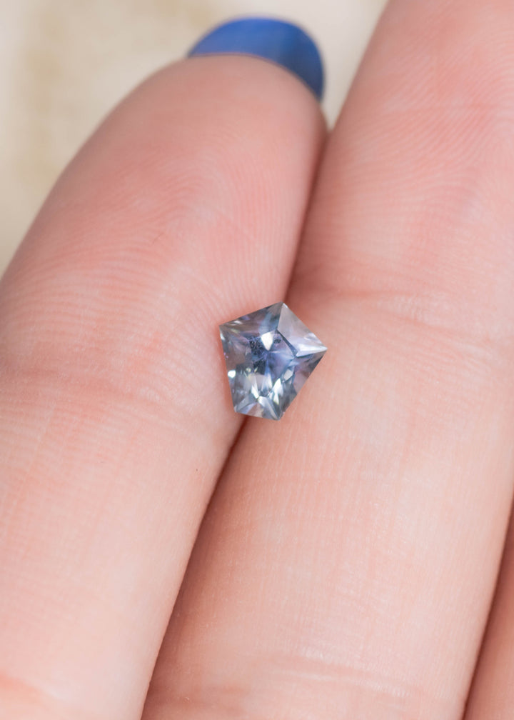 0.85 carat unheated Montana sapphire modified kite cut displayed on fingertip for scale, showing blue, green and violet brilliance from El Dorado Bar.