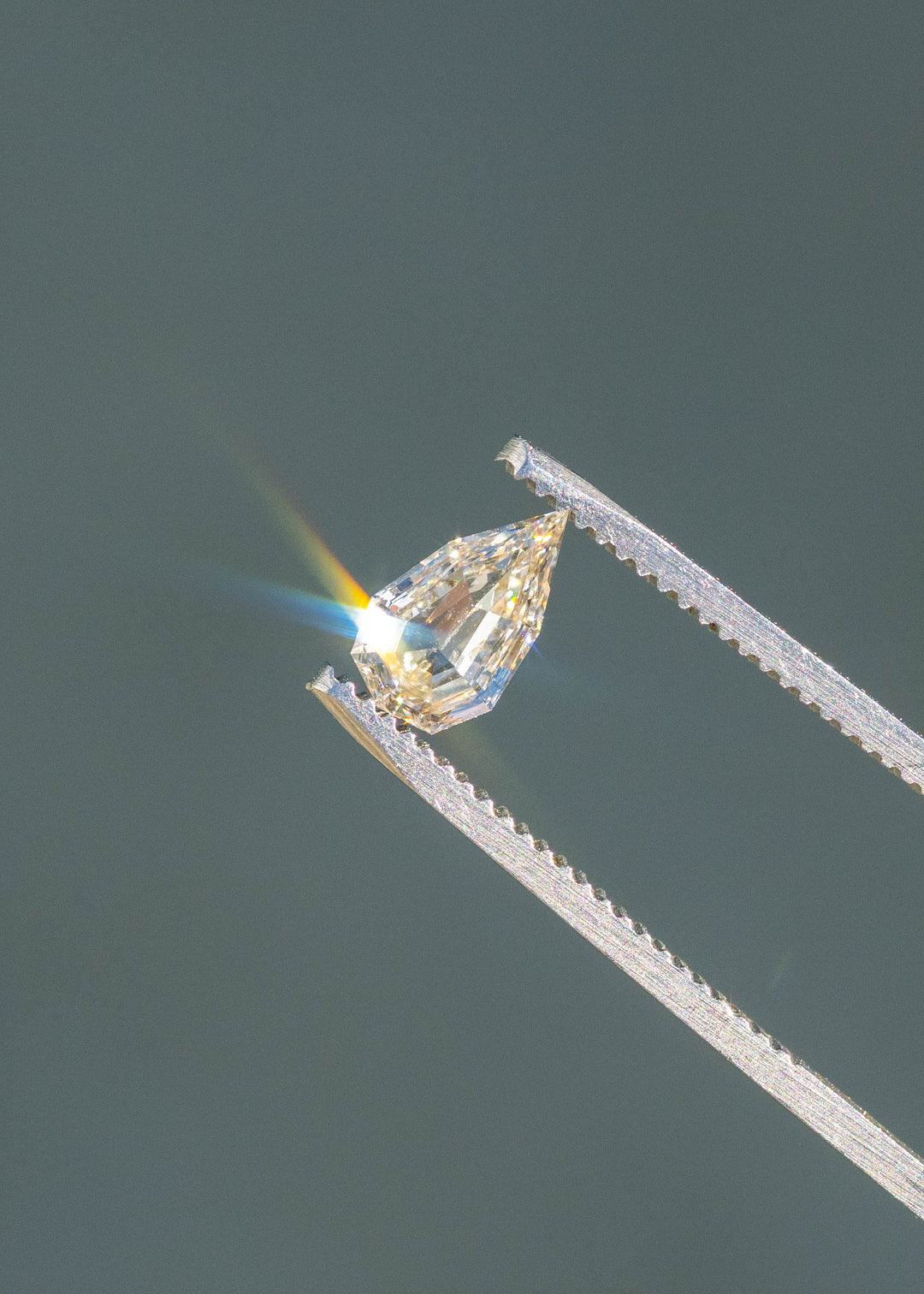 0.89ct Geo Pear Step Cut Champagne Diamond held in gem tweezers under direct sunlight reflecting rainbows off of geo pear facets.