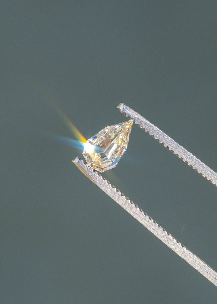 0.89ct Geo Pear Step Cut Champagne Diamond held in gem tweezers under direct sunlight reflecting rainbows off of geo pear facets.
