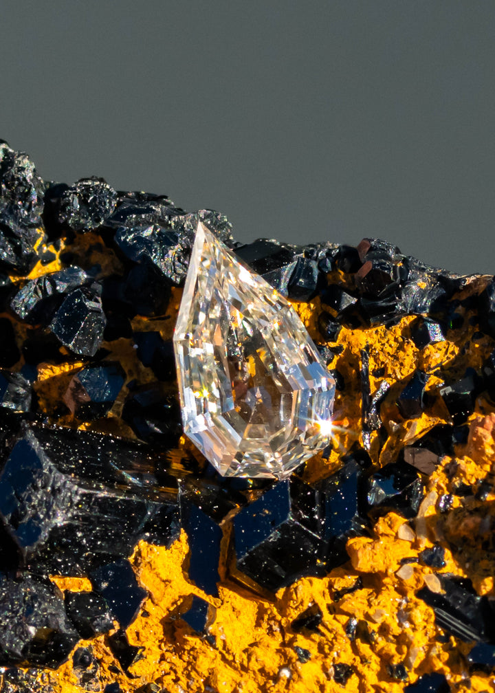 0.89ct Geo Pear Step Cut Champagne Diamond resting on natural tourmaline gemstone under direct sunlight.