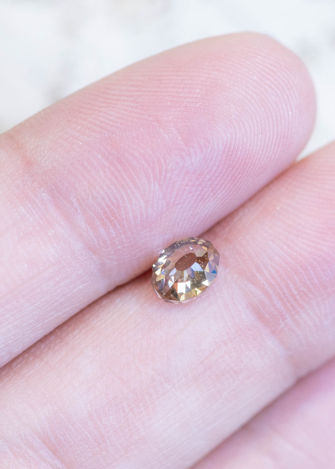 Loose fancy light brown champagne diamond in Mughal cut resting on fingertips, showing its size, warm color, and unique faceting pattern.