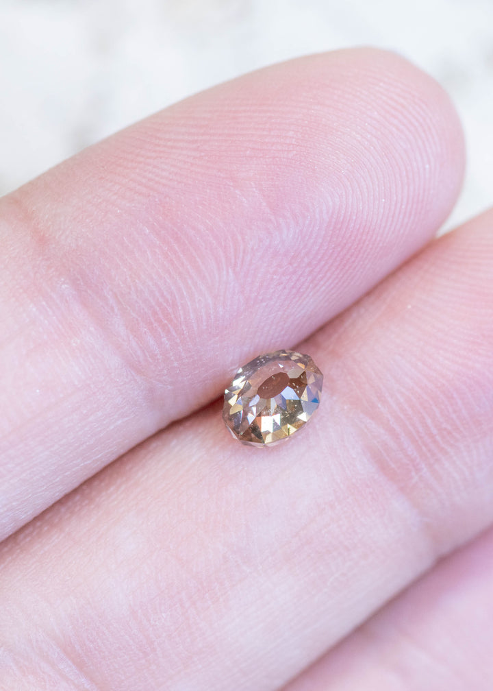 Loose fancy light brown champagne diamond in Mughal cut resting on fingertips, showing its size, warm color, and unique faceting pattern.