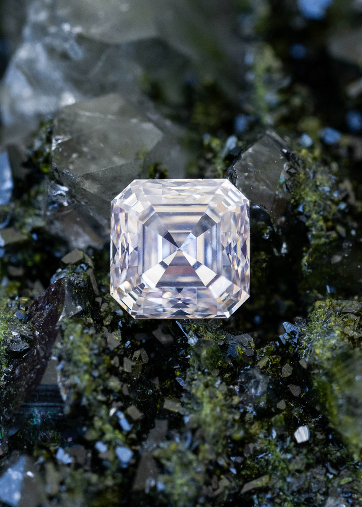 0.90 carat M color VVS1 Asscher cut Canadian diamond resting on dark green mineral crystals, showing its square outline, clipped corners and geometric step facets.