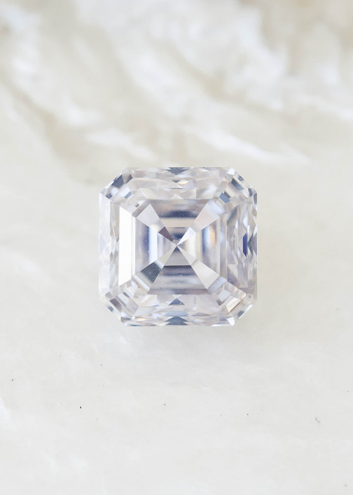 Face-up 0.90 carat natural Asscher cut diamond on a pale background, displaying its warm ivory tone, concentric step facets and symmetrical central cross.