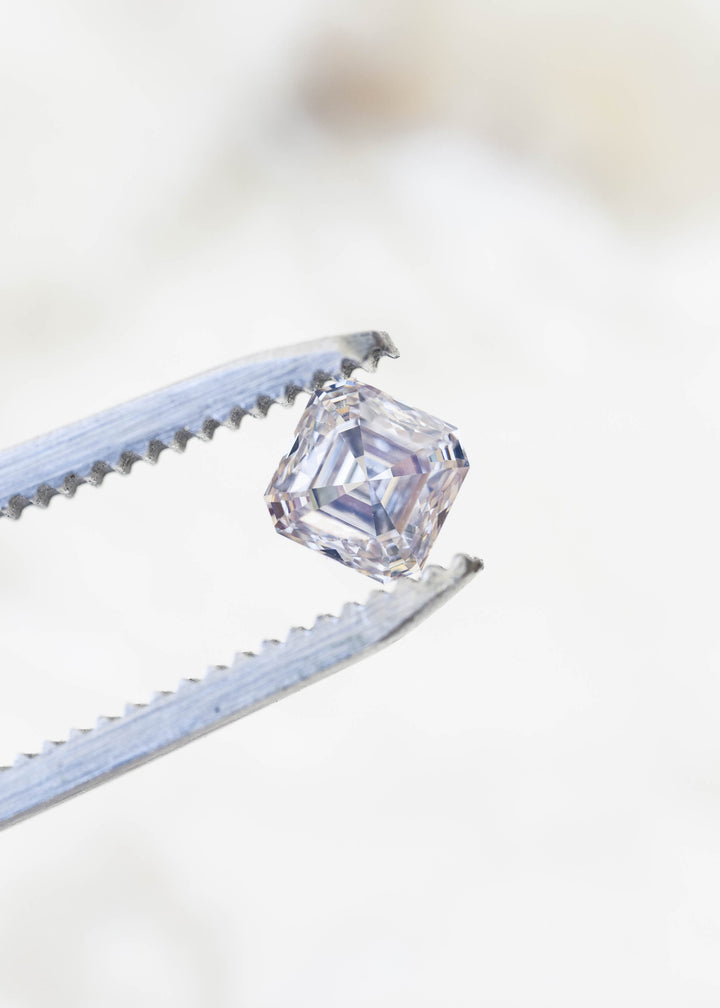 Angled macro view of the Canadian Asscher cut diamond held in jeweler’s tweezers, revealing its clipped corners, depth and layered step-cut architecture.