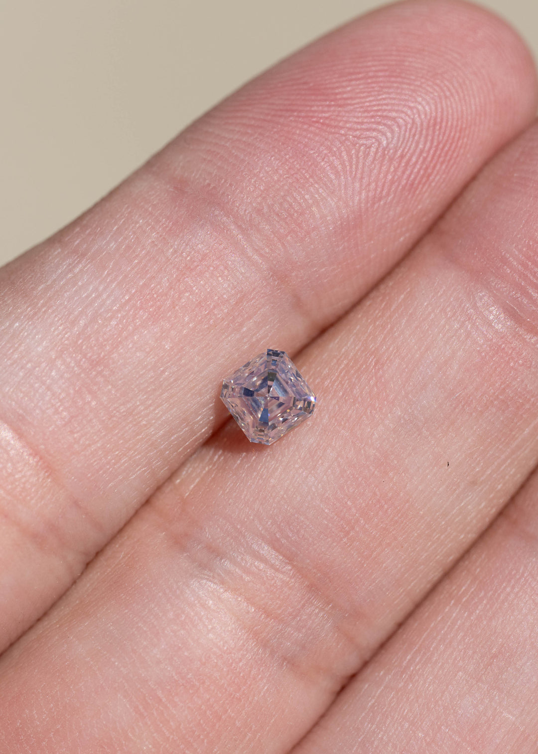Face-up view of the M color VVS1 Asscher cut diamond on a hand, showing crisp geometric facets and subtle champagne and silver reflections.