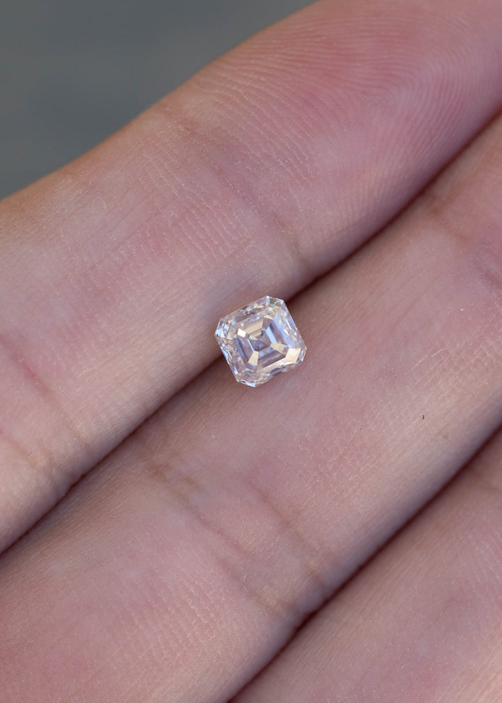 0.90 carat Asscher cut diamond resting on a hand for scale, showing its compact square proportions and warm M color.