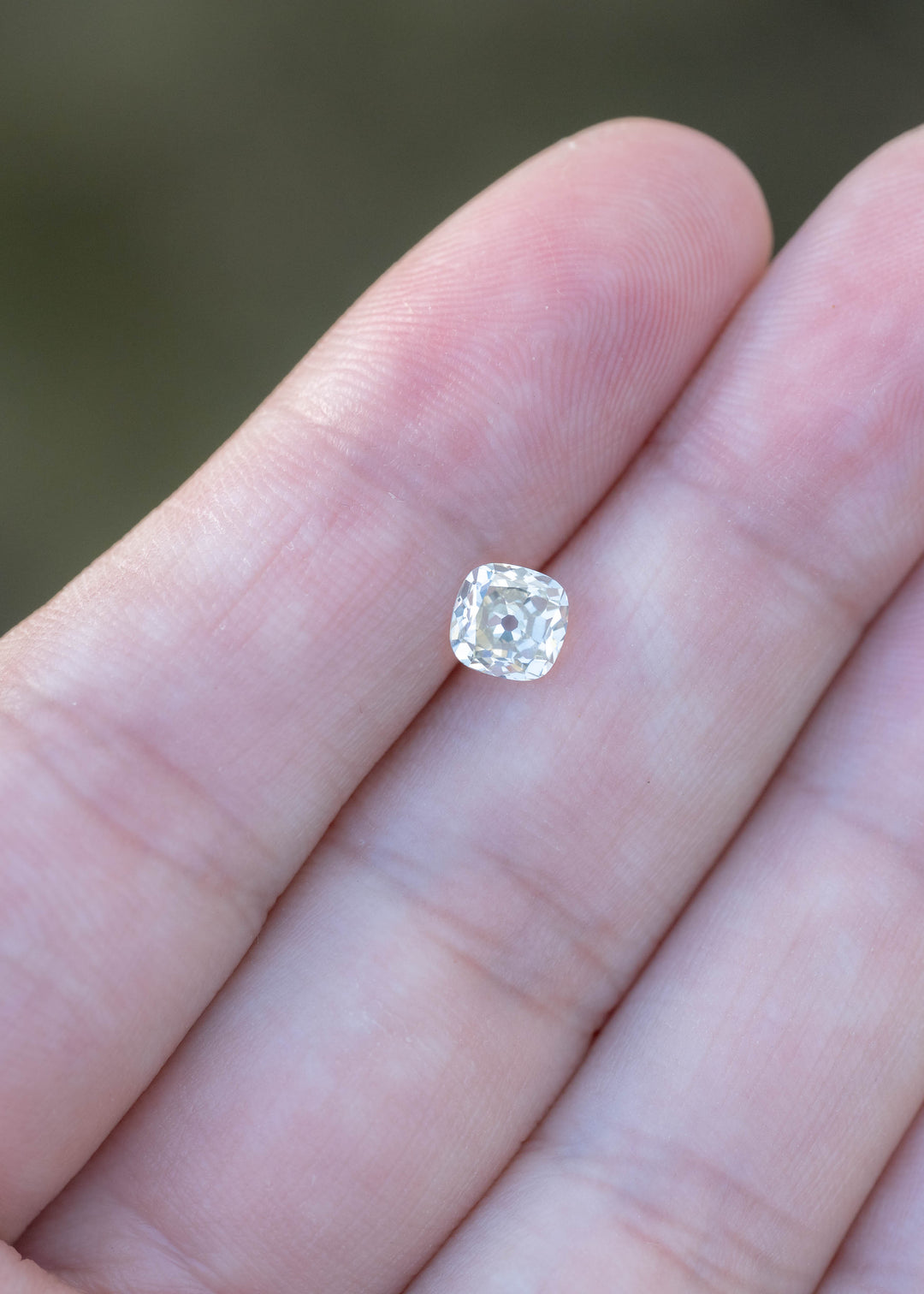 0.92 carat white antique-style cushion diamond resting on fingertips for scale, revealing its softly rounded square outline and heirloom-inspired faceting.