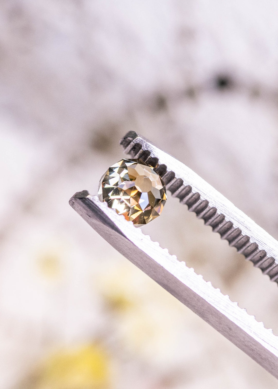 Fancy yellow brown Mughal cut diamond held in metal tweezers, highlighting brilliant champagne reflections and symmetrical round shape.