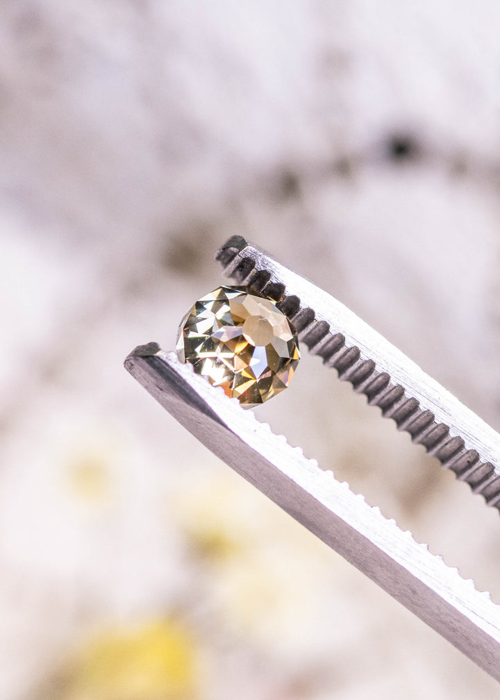 Fancy yellow brown Mughal cut diamond held in metal tweezers, highlighting brilliant champagne reflections and symmetrical round shape.