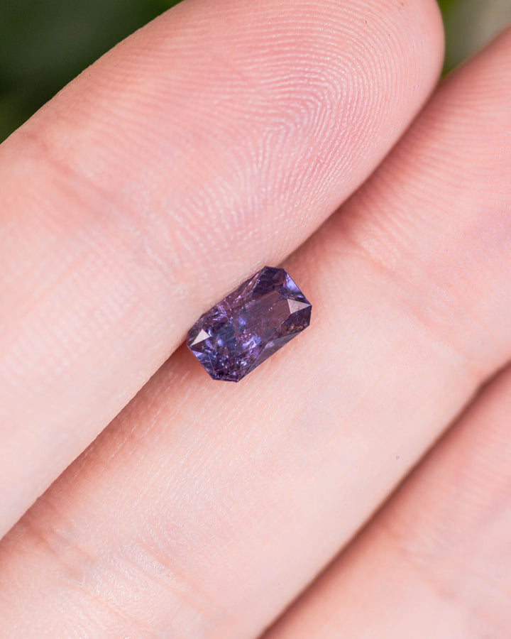 0.94 carat gray and purple sapphire balanced on fingertip, showing detailed brilliance and symmetry of its custom radiant cut, untreated gem from Umba River Valley, Tanzania.