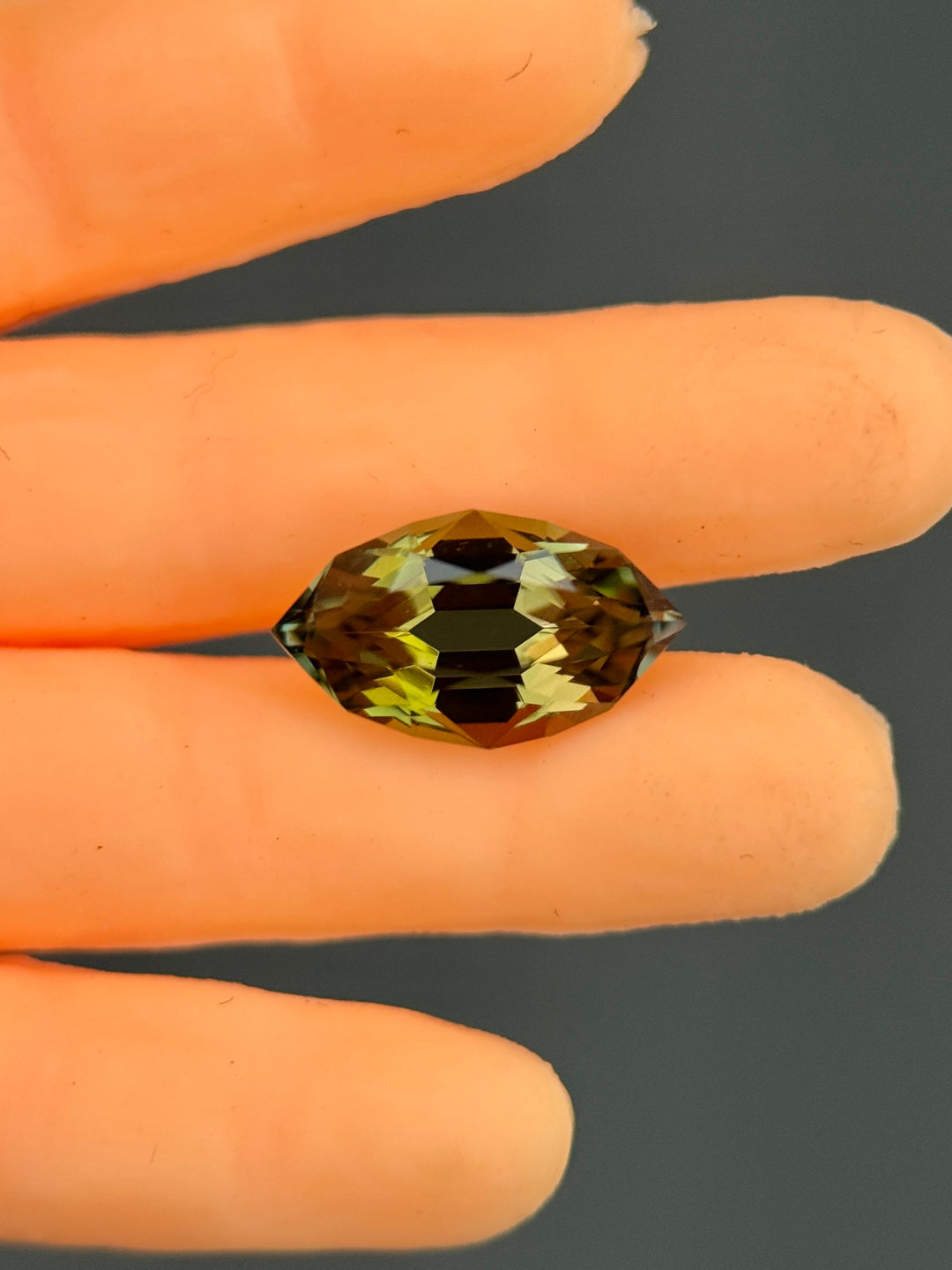 0.94-carat olive green tanzanite held between fingers, showing its custom antique style cut and natural untreated color. Merelani Hills Tanzanite photographed in bright lighting to highlight faceting and brilliance.