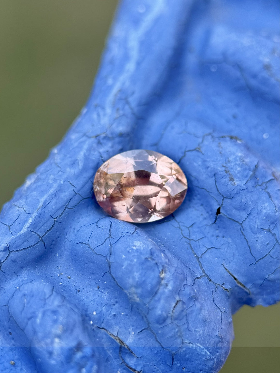 Macro photo of a 0.95ct oval mix cut sapphire with color change from peach to pink, resting on blue textured background – Umba River, Tanzania.