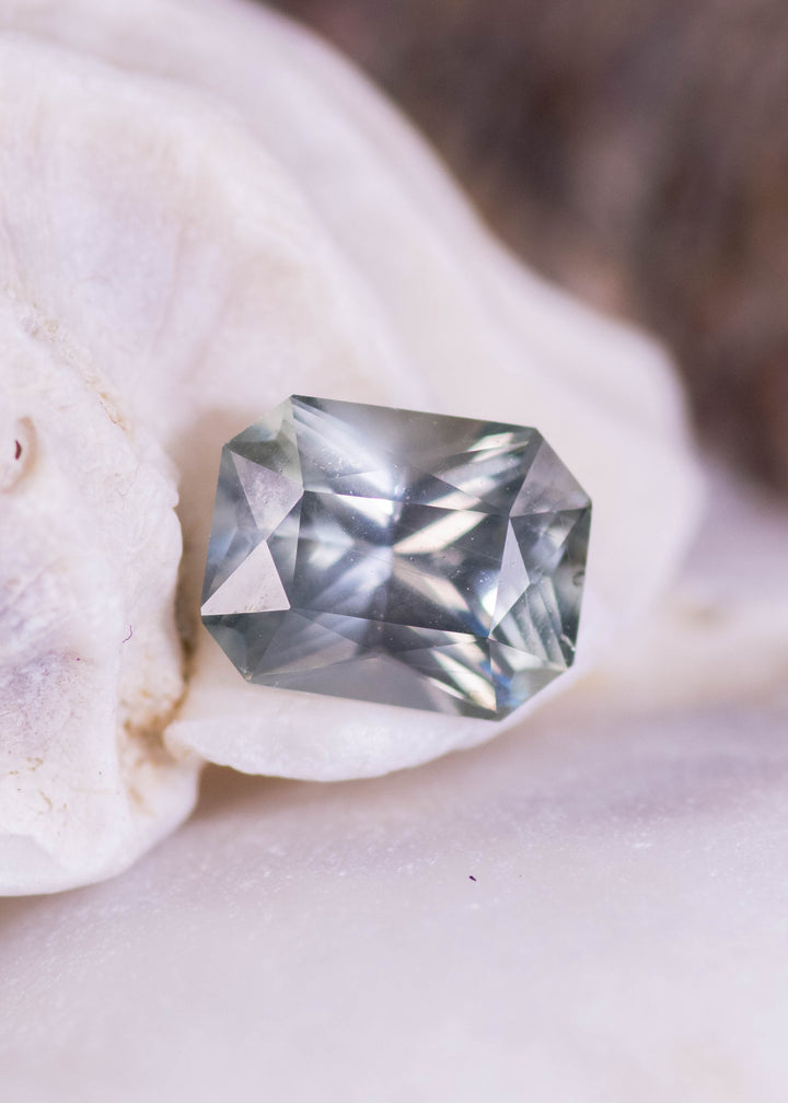 Teal gray blue Montana sapphire 0.96ct mixed radiant cut resting on natural quartz matrix, showing brilliant facet reflections and untreated clarity from El Dorado Bar Deposit.