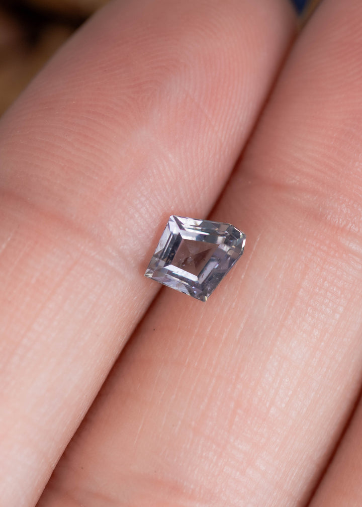 0.98 carat gray violet teal sapphire displayed on finger for scale, unheated Montana gemstone with custom modified shield kite step cut faceting