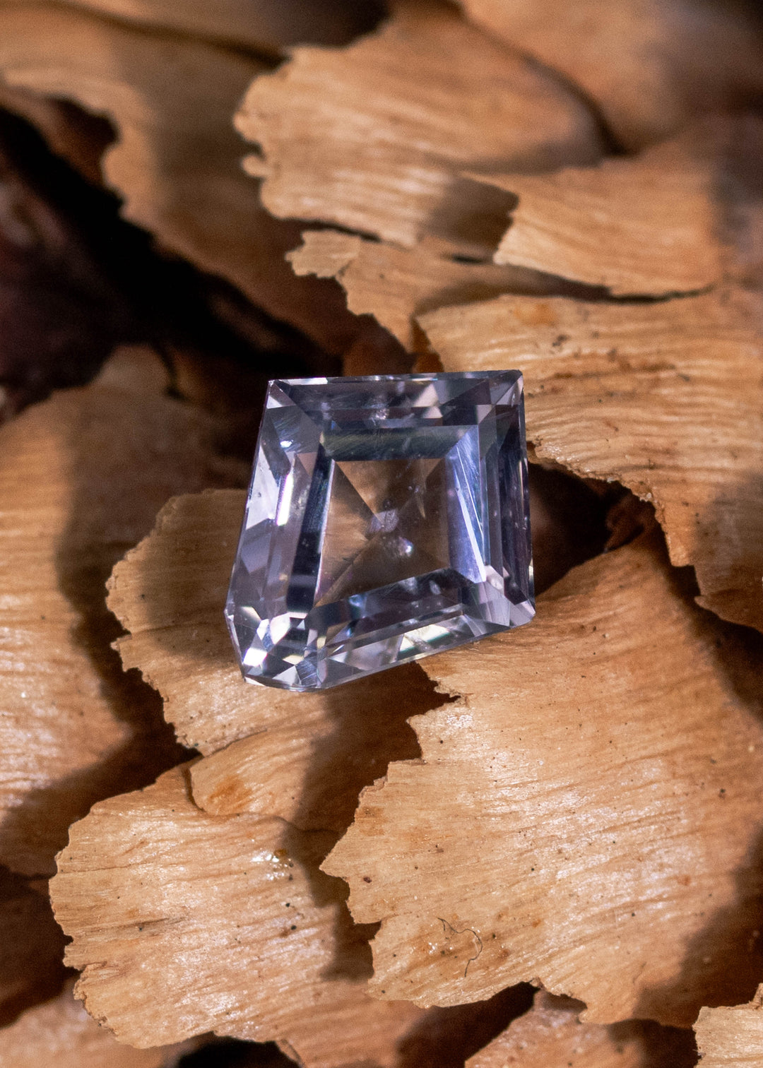 0.98 carat unheated Montana sapphire resting on natural wood, gray violet teal custom modified kite step cut from El Dorado Bar Deposit showing geometric step faceting