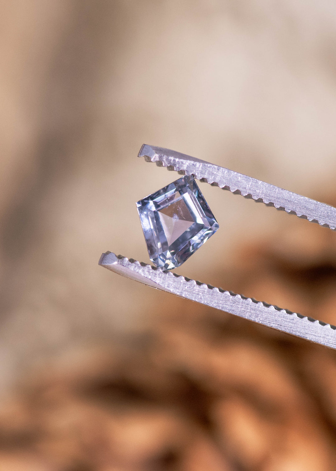 0.98ct gray violet teal Montana sapphire held in tweezers, custom modified kite step cut displaying crisp step facets and natural Montana color shift