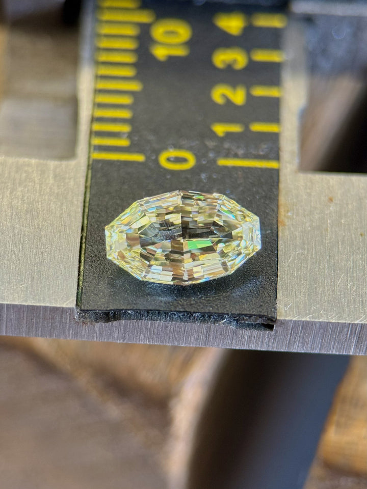 Macro shot of a 0.99 carat light yellow diamond from Gahcho Kué, Canada, on a metal measuring scale. The antique moval step cut showcases crisp lines and fine brilliance, highlighting its VVS1 clarity and untreated origin.