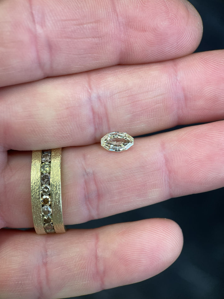 Natural 0.99 carat light yellow diamond from Gahcho Kué, Canada, resting on a fingertip beside a gold ring. The antique-style moval step cut shows precise symmetry and high clarity, graded VVS1, untreated and ethically sourced.