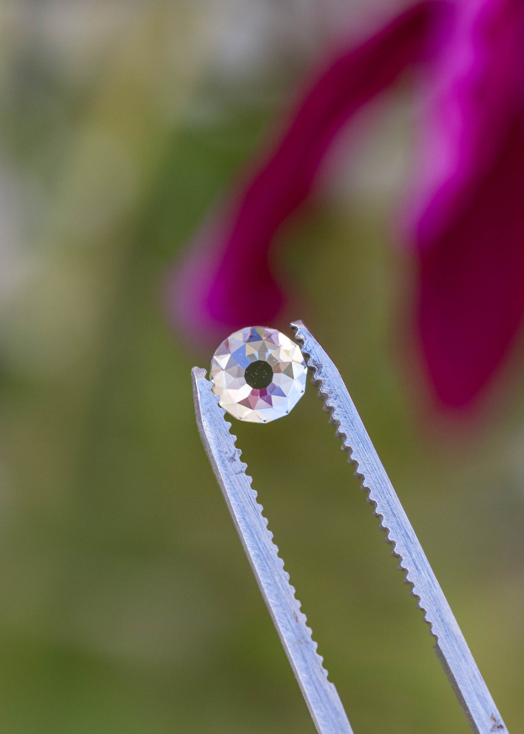 Face-up round Mughal cut diamond between jeweler’s tweezers, with broad geometric facets reflecting white, blue and subtle warm tones.