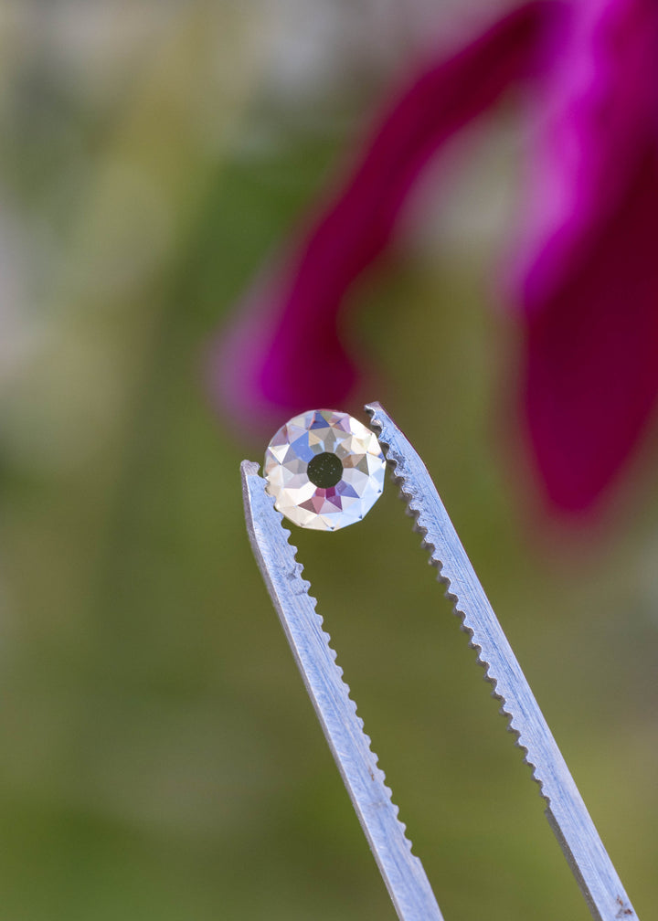 Face-up round Mughal cut diamond between jeweler’s tweezers, with broad geometric facets reflecting white, blue and subtle warm tones.