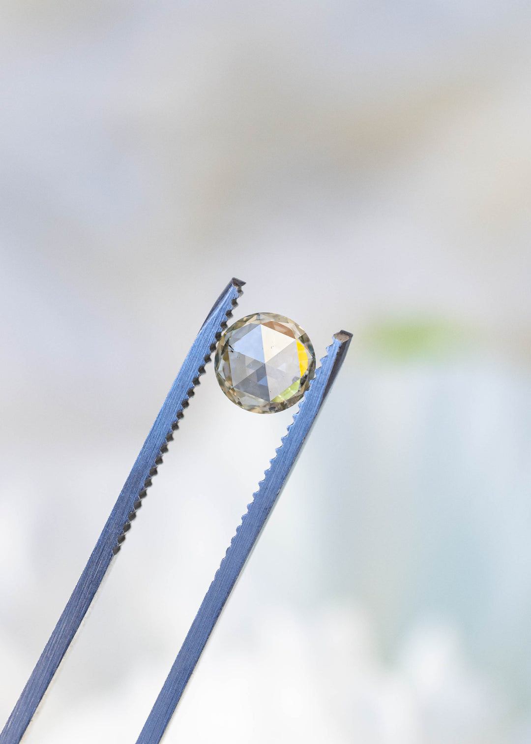 Natural 1.00 carat grey champagne rose cut diamond held in gem tweezers, highlighting its symmetrical round shape, low-profile rose cut, and subtle champagne reflections.